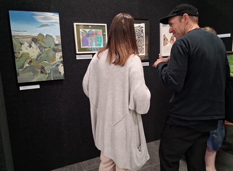 Two people looking at art on the wall before the auction begins